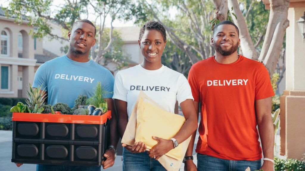 Diverse delivery team smiling with packages on a sunny day in a neighborhood.